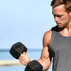 Mężczyzna ćwiczy biceps na świeżym powietrzu, podnosząc ciężarek. Zastanawia się, ile serii na biceps wykonać dzisiaj.