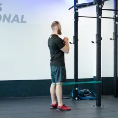 Mężczyzna wykonuje ćwiczenie spanish squat z gumą oporową wokół ud, przygotowując się do przysiadu.