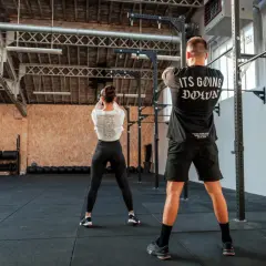 Para pozuje na siłowni. Ona wykonuje ćwiczenie z kettlebell, on stoi z tyłu. To właśnie crossfit co to za trening!