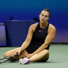 Zmęczona tenisistka siedzi na korcie, trzymając rakietę. Intensywny mecz tenis kobiet.