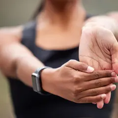 Kobieta rozciąga rękę, delikatnie masując nadgarstek. Na jej lewej ręce widoczny jest smartwatch.