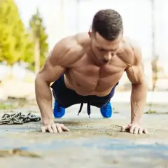 Mięśniowy mężczyzna wykonuje pompki na biceps, z łańcuchem obok.