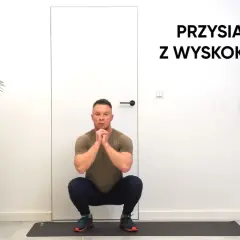 Mężczyzna w pozycji do przysiadów z wyskokiem, gotowy do ćwiczeń.