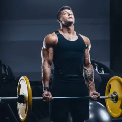 Mięśniowy mężczyzna wykonuje ćwiczenie na biceps z ciężarem. Jego **split trening** przynosi efekty.