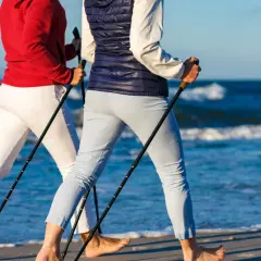 Dwie osoby uprawiające chodzenie z kijkami na plaży, z morzem w tle.