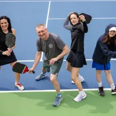 Rodzina na korcie do pickleball, co to za sport? Wszyscy trzymają rakietki, gotowi do gry.