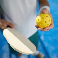 Gracz trzyma rakietkę i żółtą piłeczkę. Idealny sprzęt do treningu mobility i gry w pickleball.