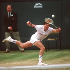 Jimmy Connors w akcji, uderza piłkę na trawiastym korcie. W tle sędzia i chłopiec podający piłki.