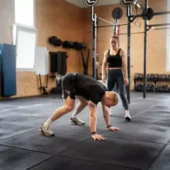 Trenerka obserwuje mężczyznę wykonującego burpee, ćwiczenie znane z intensywności.
