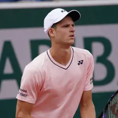 Hubert Hurkacz w różowej koszulce i białej czapce z logo Yonex, gotowy do gry na korcie.