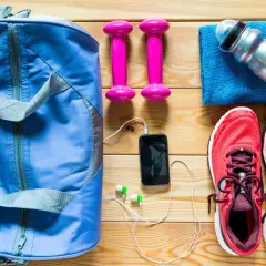 Niebieska torba sportowa, różowe hantle, czerwone buty, telefon ze słuchawkami i butelka wody – to wszystko, co zabrać na siłownię.