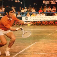 Ken Rosewall w akcji na korcie, w pomarańczowej koszulce i białych spodenkach, podczas meczu U.S. Open.