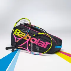 Dwie kolorowe rakiety tenisowe, jakich używałby Rafael Nadal, leżą obok czarnej torby z logo Babolat.