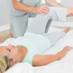 Fizjoterapeuta wykonuje test obera na leżącej kobiecie, sprawdzając ruchomość jej biodra.