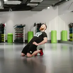 Mężczyzna wykonuje ćwiczenie nordic curl, klęcząc na podłodze i pochylając się do przodu.