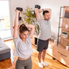 Para ćwiczy ćwiczenia na triceps w domu, podnosząc hantle nad głowę.