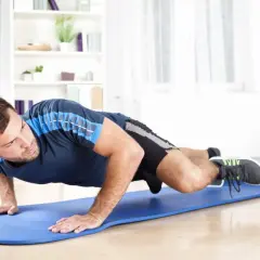 Mężczyzna wykonuje trening siłowy w domu, ćwicząc na niebieskiej macie.