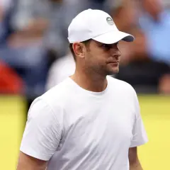 Andy Roddick w białej czapce z logo US Open i białej koszulce, zapatrzony w dal.