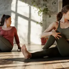 Dwie kobiety wykonują skręt tułowia na macie. To ćwiczenie to stretching, który poprawia elastyczność.