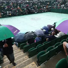 Wimbledon deszcz przerwał mecz. Widzowie siedzą pod parasolami, a kort przykryty jest plandeką.