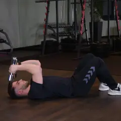 Mężczyzna wykonuje francuskie wyciskanie hantli leżąc na podłodze. Ćwiczenie na triceps.