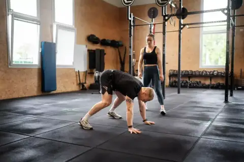Trenerka obserwuje mężczyznę wykonującego burpee, ćwiczenie znane z intensywności.