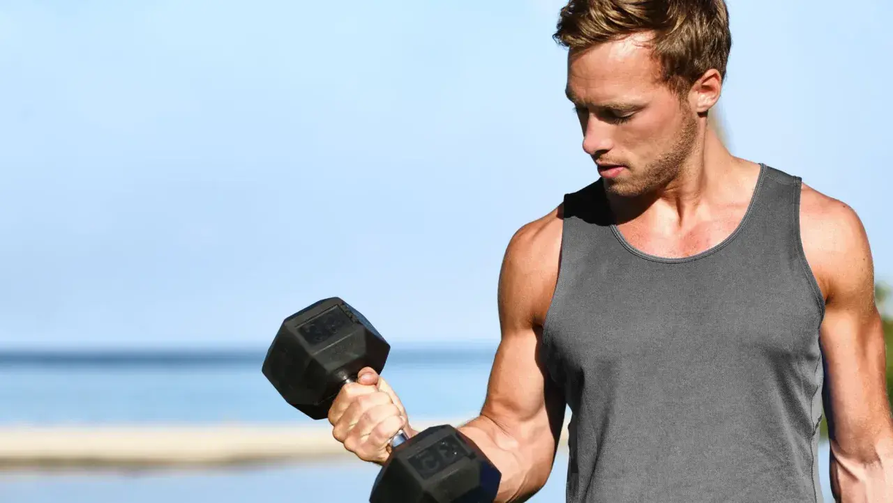 Mężczyzna ćwiczy biceps na świeżym powietrzu, podnosząc ciężarek. Zastanawia się, ile serii na biceps wykonać dzisiaj.