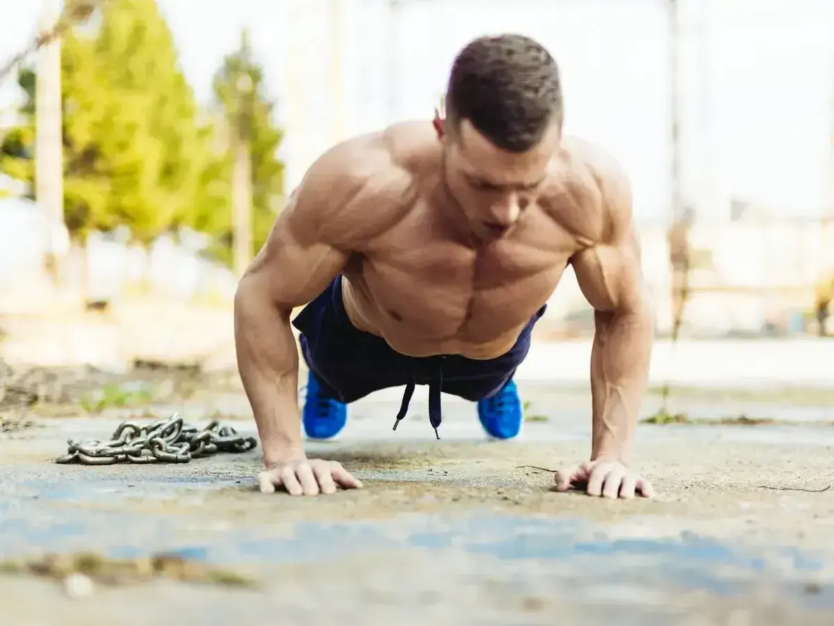 Mięśniowy mężczyzna wykonuje pompki na biceps, z łańcuchem obok.