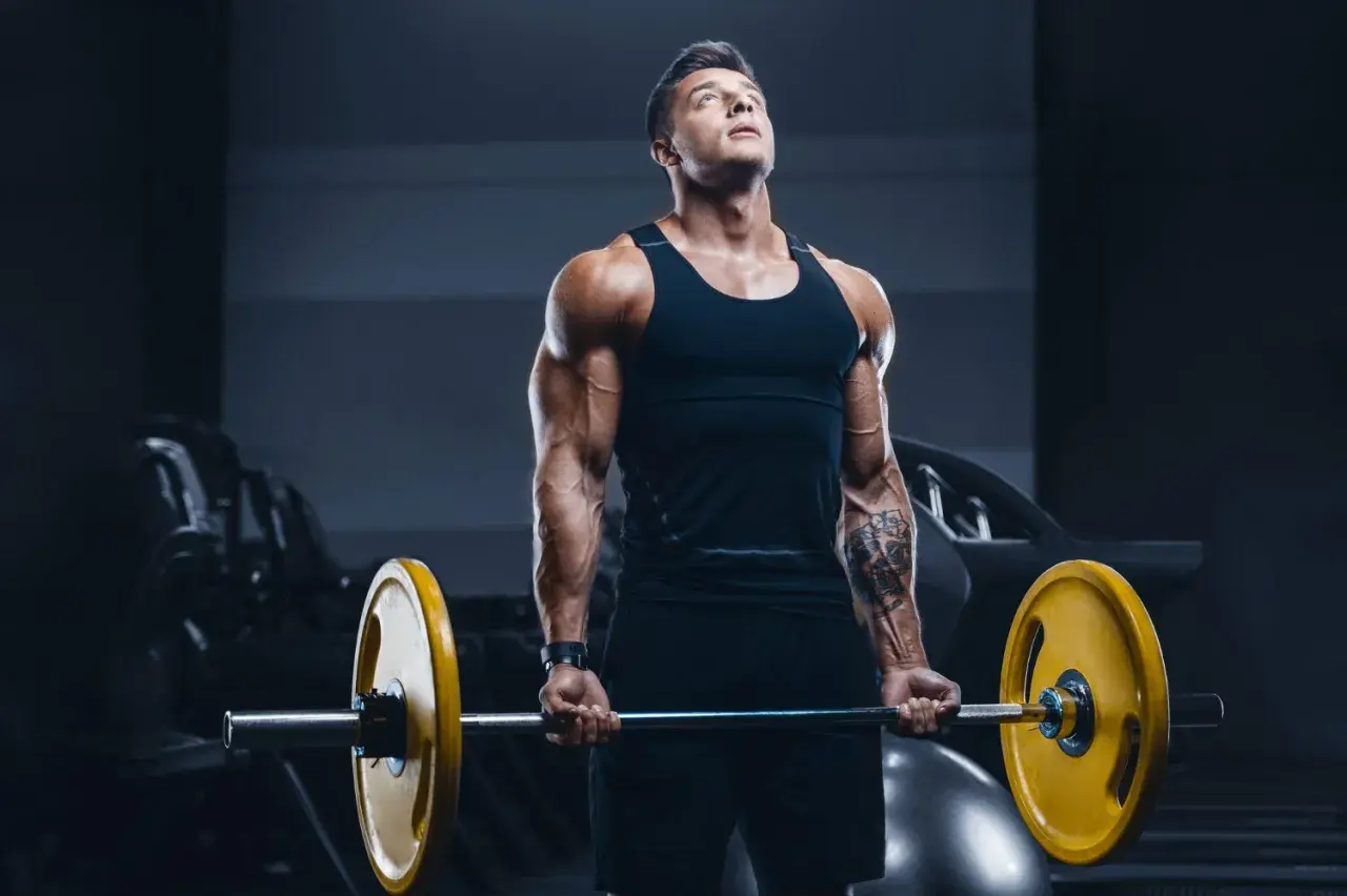Mięśniowy mężczyzna wykonuje ćwiczenie na biceps z ciężarem. Jego **split trening** przynosi efekty.