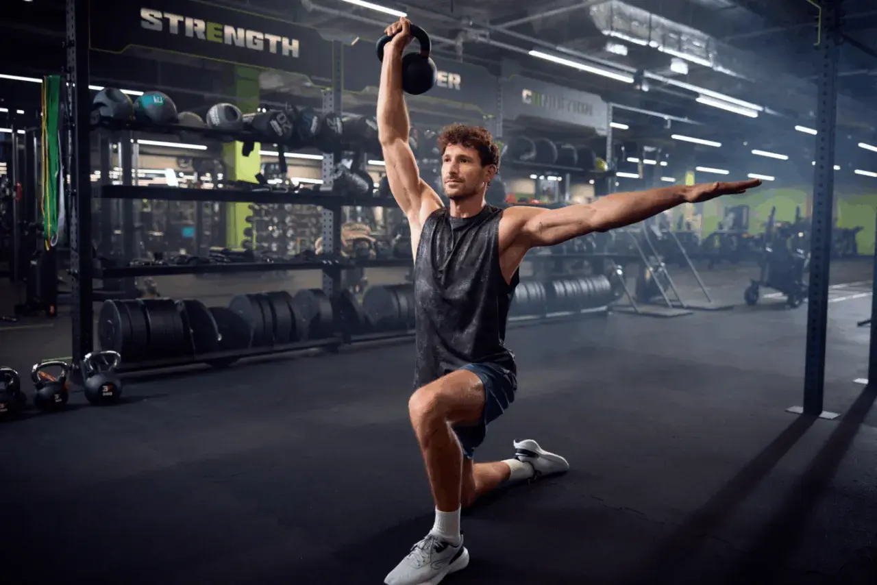 Mężczyzna wykonuje ćwiczenie z kettlebell w siłowni. To część jego zajęć tbc.