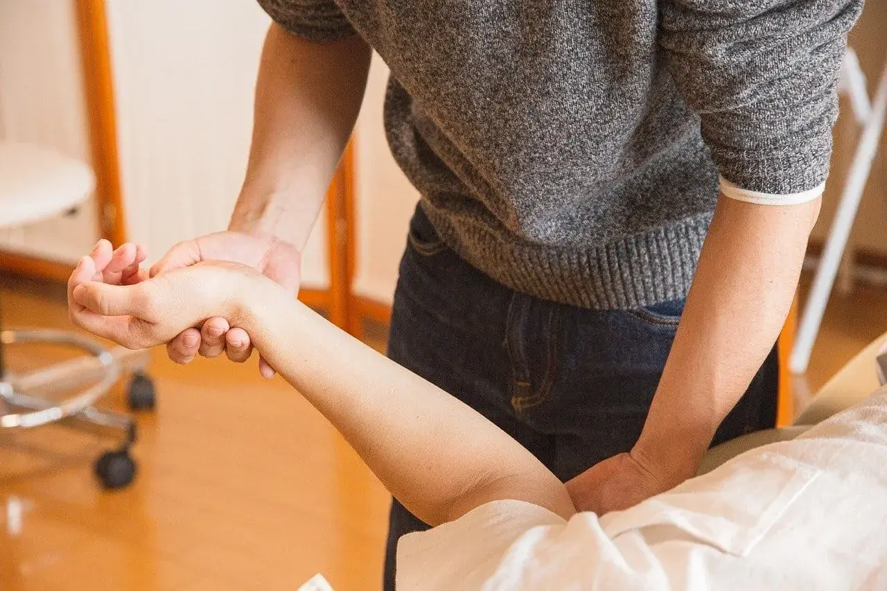 Fizjoterapeuta delikatnie masuje przedramię pacjenta, pokazując, jak leczyć łokieć tenisisty.