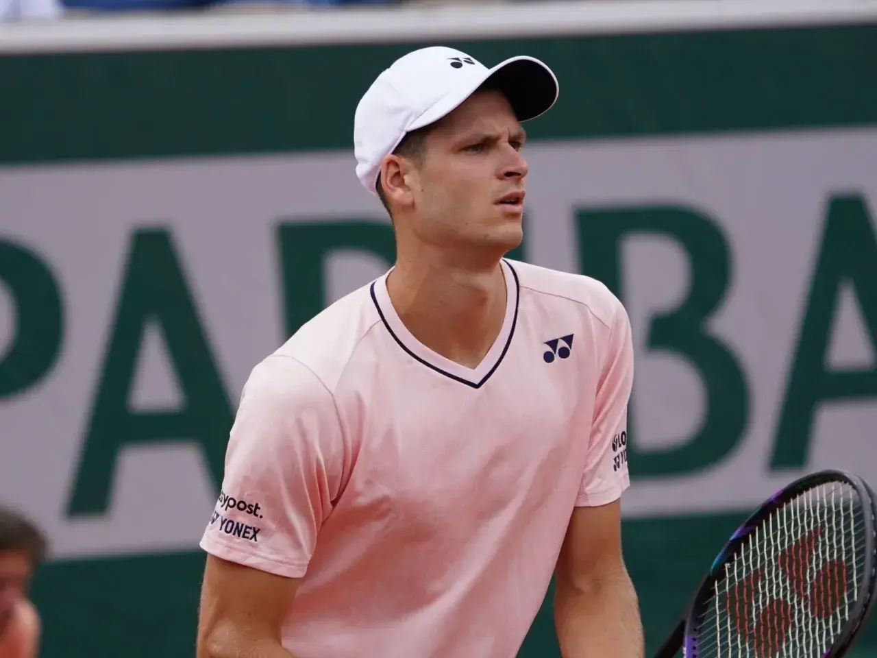 Hubert Hurkacz w różowej koszulce i białej czapce z logo Yonex, gotowy do gry na korcie.