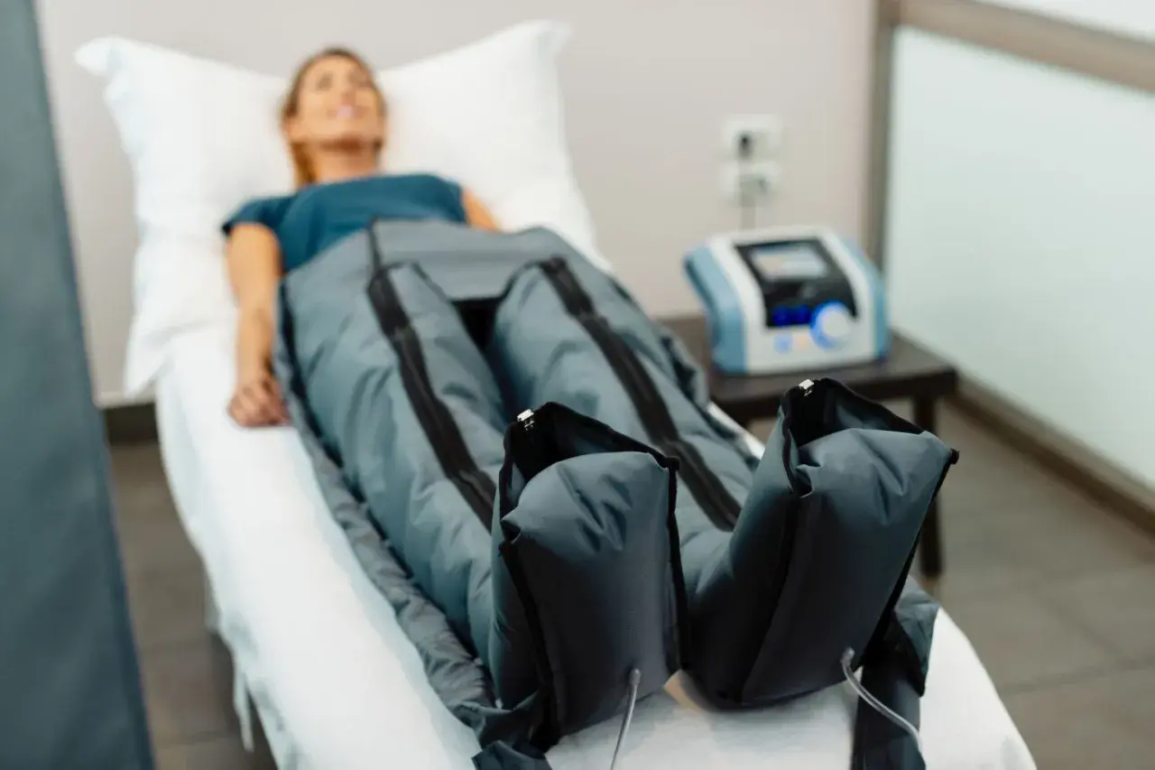 Kobieta leży na łóżku, jej nogi są w specjalnych mankietach. To presoterapia, zabieg poprawiający krążenie.