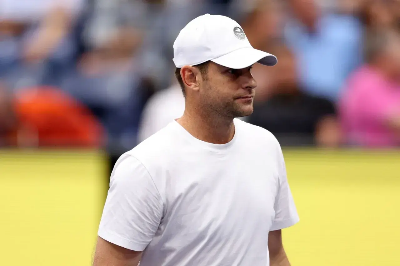 Andy Roddick w białej czapce z logo US Open i białej koszulce, zapatrzony w dal.