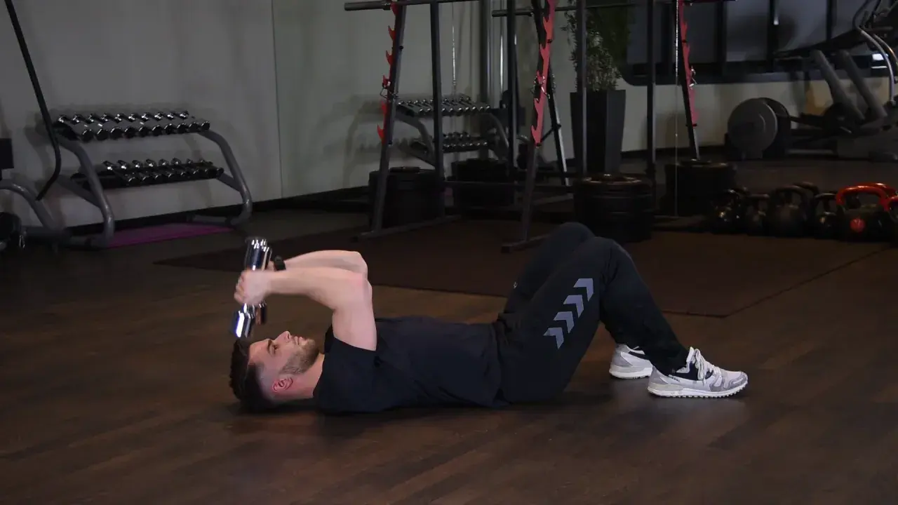 Mężczyzna wykonuje francuskie wyciskanie hantli leżąc na podłodze. Ćwiczenie na triceps.