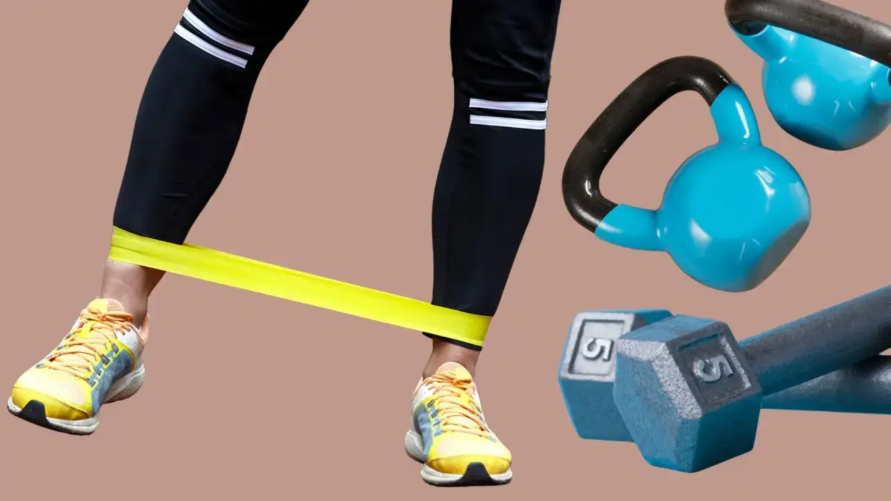 Noga w żółtej opasce ćwiczy, obok hantle i kettlebell. Efektywny trening oporowy.
