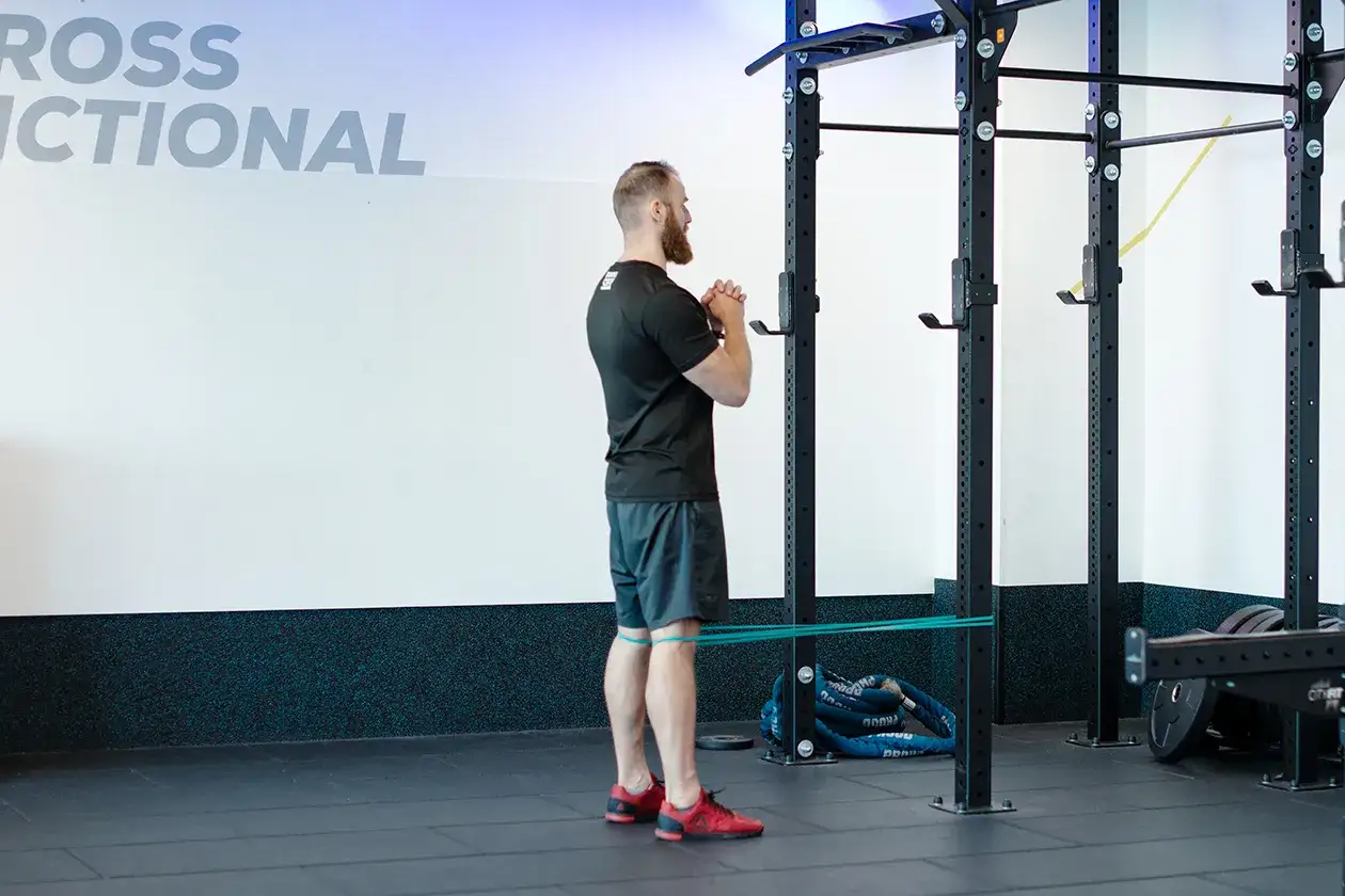 Mężczyzna wykonuje ćwiczenie spanish squat z gumą oporową wokół ud, przygotowując się do przysiadu.