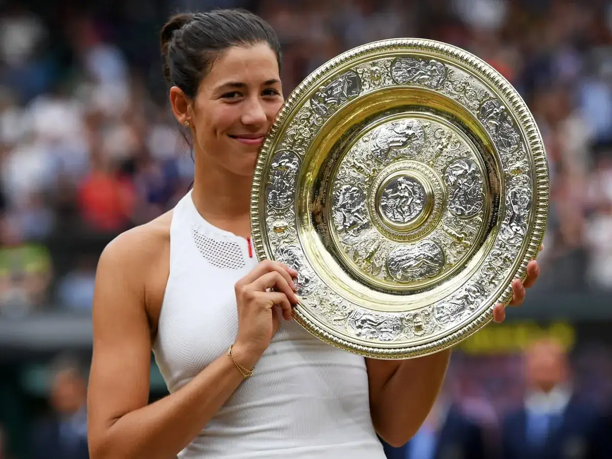 Garbine Muguruza z dumą prezentuje puchar Wimbledonu, uśmiechając się do obiektywu.