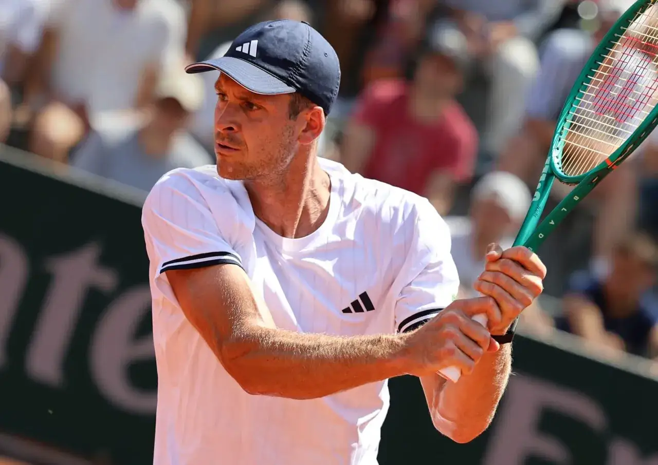Tenisista w czapce z daszkiem i białej koszulce z logo Adidasa, gotowy do uderzenia. Czy to Stefan Edberg?