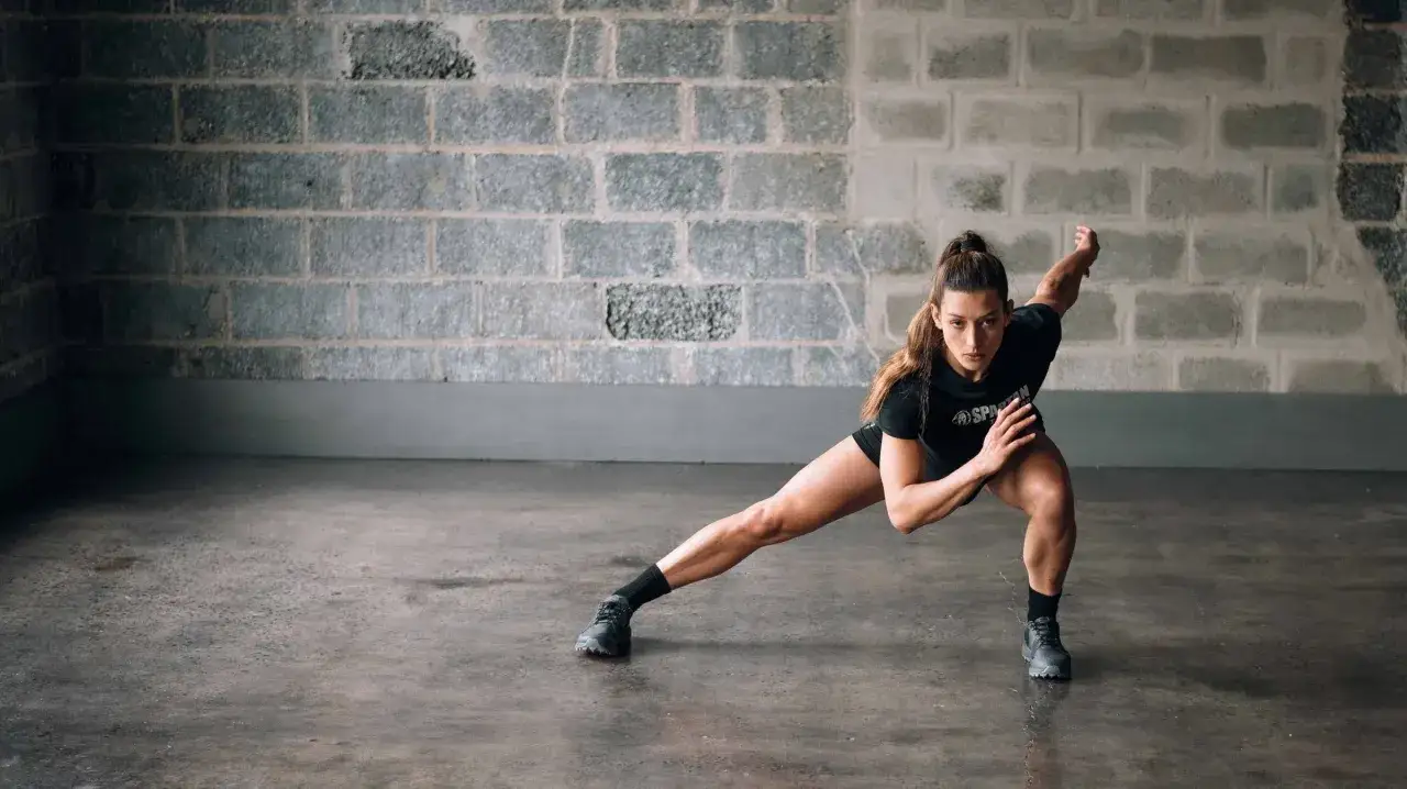 Kobieta wykonuje głęboki wykrok boczny, ćwicząc siłę i gibkość. To element intensywnego treningu crossfit.