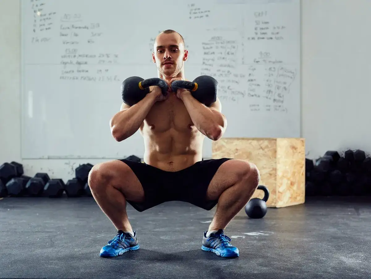 Mężczyzna wykonuje przysiady z kettlebellami, ćwicząc siłę nóg. Zastanawia się, ile przysiadów dziennie jest optymalne dla jego treningu.