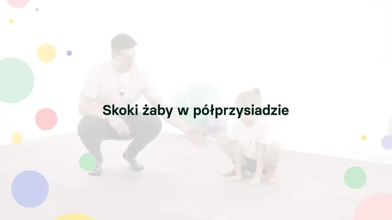 Trener zachęca dziecko do ćwiczeń, wykonując razem żabie skoki w półprzysiadzie. Kolorowe kółka dodają zabawy.