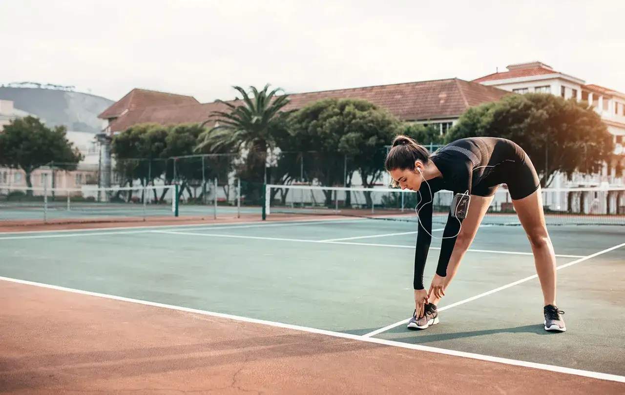Dziewczyna w sportowym stroju wykonuje rozgrzewkę dla dzieci na korcie tenisowym, słuchając muzyki.